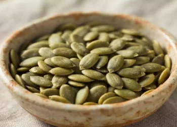Ciotola in ceramica colma di semi di zucca verdi su tavolo chiaro, alimento ricco di nutrienti spesso associato a benessere, sazietà e alimentazione equilibrata.