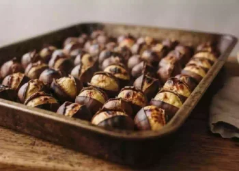 Castagne al forno appena sfornate su una teglia rustica, con buccia incisa e polpa morbida, circondate da foglie autunnali e colori caldi di stagione, perfette per una cottura gustosa e fragrante.