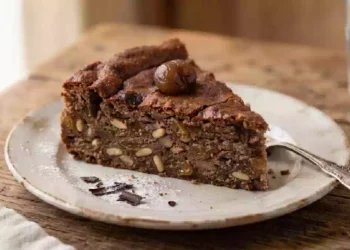 Torta di castagne con gocce di cioccolato, pinoli e uvetta servita su un piatto rustico in legno, dolce autunnale soffice e profumato ideale per la colazione o la merenda.