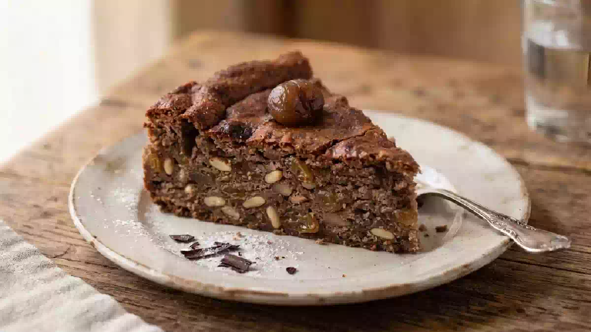 Torta di castagne con gocce di cioccolato, pinoli e uvetta servita su un piatto rustico in legno, dolce autunnale soffice e profumato ideale per la colazione o la merenda.