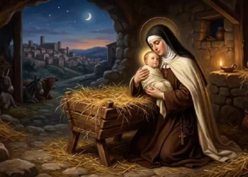 Santa Teresa d’Avila tiene in braccio Gesù Bambino accanto alla mangiatoia in una scena ispirata alla Natività, all’interno di una stalla illuminata dalla luce delle candele sotto il cielo notturno