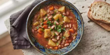 Foto di uno spezzatino vegetale con fagioli rossi, patate e peperoni in salsa cremosa, servito caldo in una ciotola rustica.