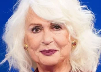 Loretta Goggi in primo piano durante un'apparizione pubblica, con capelli bianchi e sfondo blu. La celebre artista italiana ha annunciato la sua scelta di restare lontana dalla televisione
