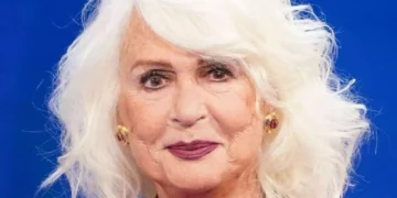 Loretta Goggi in primo piano durante un'apparizione pubblica, con capelli bianchi e sfondo blu. La celebre artista italiana ha annunciato la sua scelta di restare lontana dalla televisione
