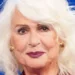 Loretta Goggi in primo piano durante un'apparizione pubblica, con capelli bianchi e sfondo blu. La celebre artista italiana ha annunciato la sua scelta di restare lontana dalla televisione