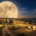 Gigantesca Luna piena del Raccolto che domina il cielo notturno sopra una campagna collinare, con casale rurale, campi dorati appena mietuti, trattore al lavoro e sentiero di campagna illuminato dalla luce lunare. Suggestiva scena autunnale che richiama le antiche tradizioni agricole legate al plenilunio di settembre.