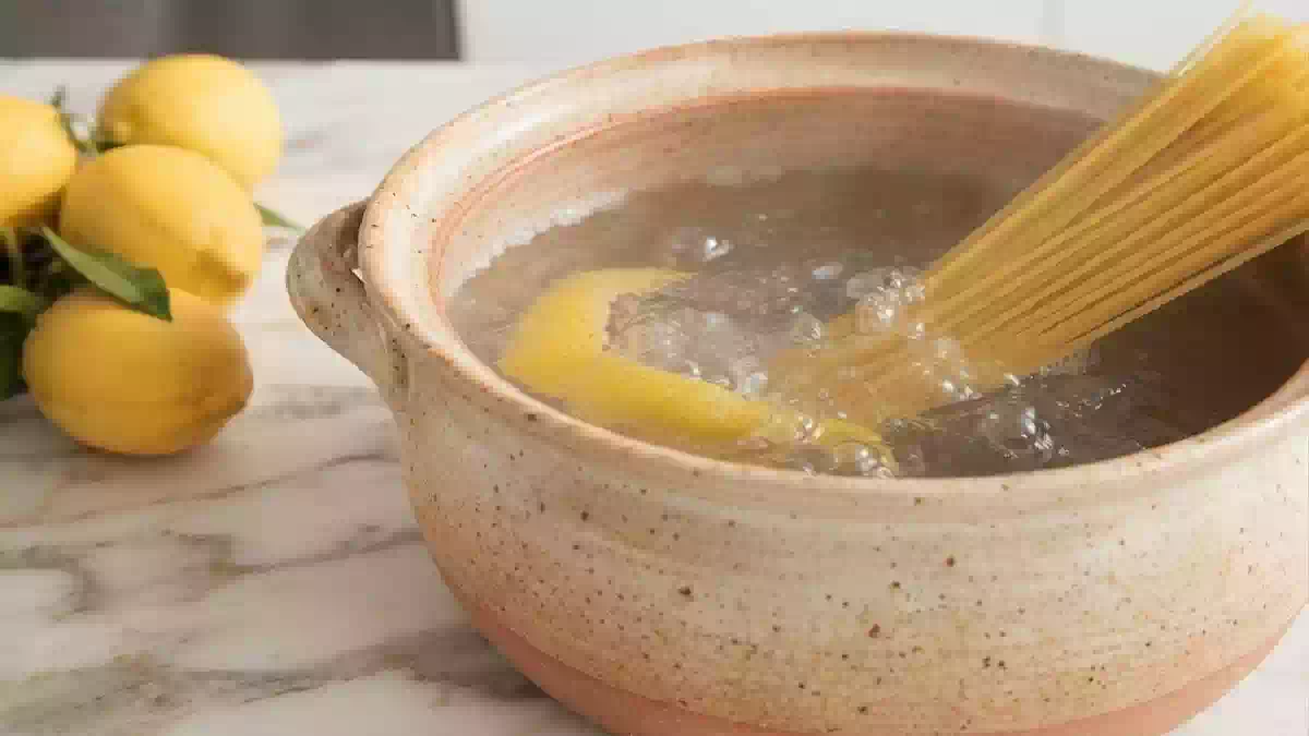 Piatto di pasta appena scolata con limone fresco accanto, simbolo del trucco per evitare che la pasta si attacchi durante la cottura.