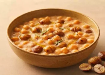 Zuppa cremosa di ceci e castagne servita in una ciotola rustica, guarnita con rosmarino, olio extravergine d'oliva e pepe nero su sfondo beige caldo.