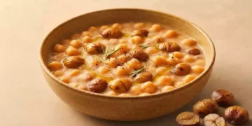 Zuppa cremosa di ceci e castagne servita in una ciotola rustica, guarnita con rosmarino, olio extravergine d'oliva e pepe nero su sfondo beige caldo.