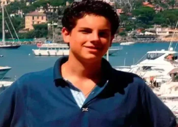 Carlo Acutis ritratto durante l'adolescenza davanti a un porto turistico, simbolo della fede e della testimonianza del giovane santo morto a 15 anni per una leucemia fulminante.