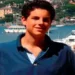 Carlo Acutis ritratto durante l'adolescenza davanti a un porto turistico, simbolo della fede e della testimonianza del giovane santo morto a 15 anni per una leucemia fulminante.