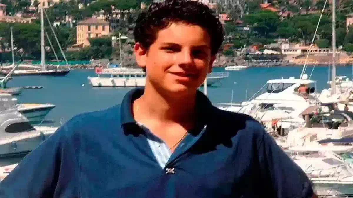 Carlo Acutis ritratto durante l'adolescenza davanti a un porto turistico, simbolo della fede e della testimonianza del giovane santo morto a 15 anni per una leucemia fulminante.