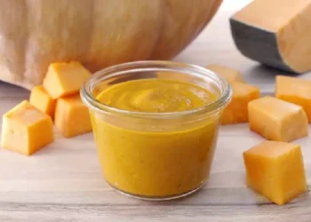 Pesto di zucca fatto in casa in vasetto di vetro con cubetti di zucca fresca su tagliere di legno, ideale per condire pasta, risotti e bruschette autunnali.