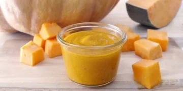Pesto di zucca fatto in casa in vasetto di vetro con cubetti di zucca fresca su tagliere di legno, ideale per condire pasta, risotti e bruschette autunnali.