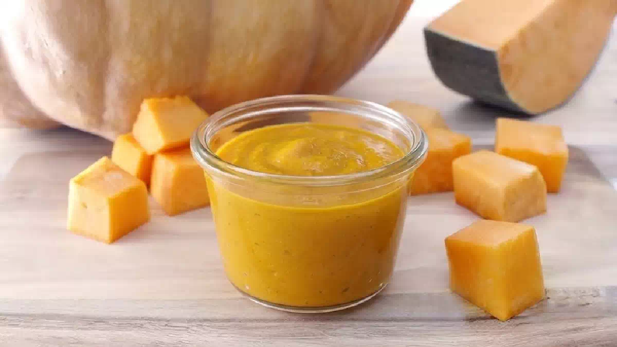 Pesto di zucca fatto in casa in vasetto di vetro con cubetti di zucca fresca su tagliere di legno, ideale per condire pasta, risotti e bruschette autunnali.