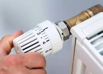 Mano che regola la valvola termostatica di un termosifone domestico per l'accensione del riscaldamento durante la stagione autunnale.