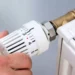 Mano che regola la valvola termostatica di un termosifone domestico per l'accensione del riscaldamento durante la stagione autunnale.