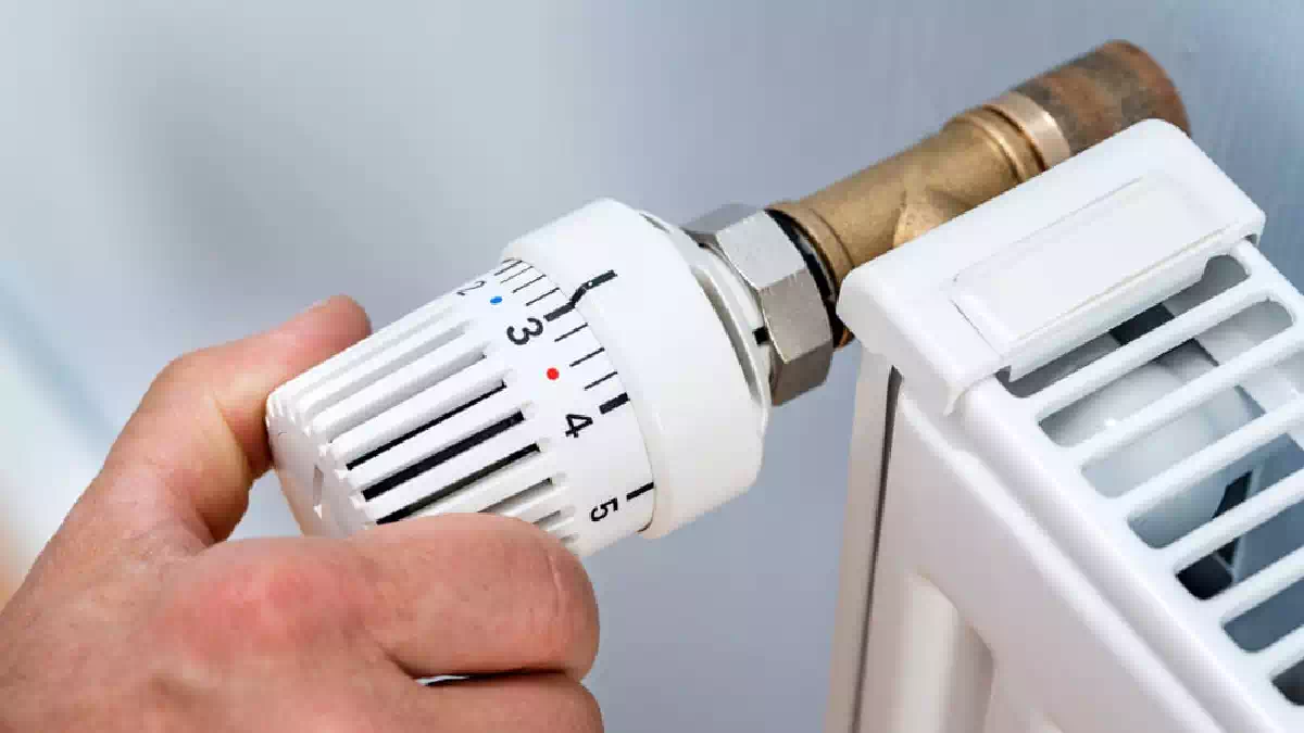 Mano che regola la valvola termostatica di un termosifone domestico per l'accensione del riscaldamento durante la stagione autunnale.