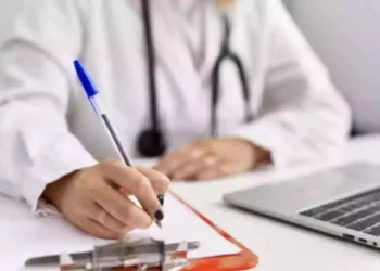 Medico compila una prescrizione sanitaria su una scrivania con computer portatile, immagine rappresentativa dell'aumento dei ticket sanitari e delle nuove tariffe del Servizio sanitario nazionale per visite specialistiche ed esami diagnostici.