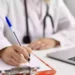 Medico compila una prescrizione sanitaria su una scrivania con computer portatile, immagine rappresentativa dell'aumento dei ticket sanitari e delle nuove tariffe del Servizio sanitario nazionale per visite specialistiche ed esami diagnostici.