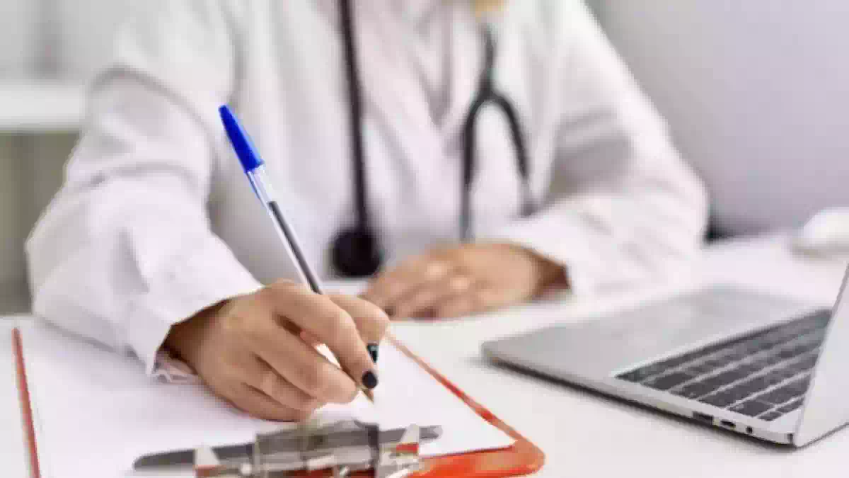 Medico compila una prescrizione sanitaria su una scrivania con computer portatile, immagine rappresentativa dell'aumento dei ticket sanitari e delle nuove tariffe del Servizio sanitario nazionale per visite specialistiche ed esami diagnostici.
