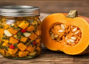 Barattolo di zucca sott’olio fatto in casa su tavolo rustico, accanto a una zucca aperta a metà, conserva autunnale tradizionale delle nonne