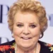 itratto ravvicinato di Wilma De Angelis durante un evento pubblico, con giacca a fantasia floreale, collana di perle e sfondo chiaro sfocato