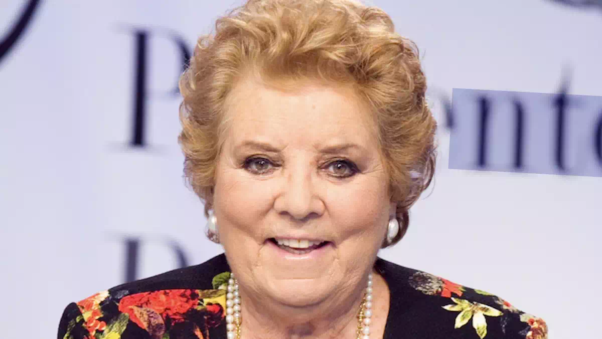 itratto ravvicinato di Wilma De Angelis durante un evento pubblico, con giacca a fantasia floreale, collana di perle e sfondo chiaro sfocato