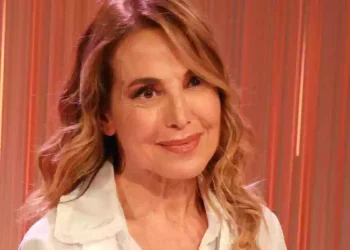 Barbara D’Urso in primo piano durante un evento televisivo, con sfondo illuminato da luci arancioni e rosse