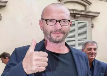 Biagio Antonacci durante una cerimonia pubblica a Rozzano, ritratto in primo piano con il pollice alzato davanti a un edificio della città