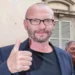 Biagio Antonacci durante una cerimonia pubblica a Rozzano, ritratto in primo piano con il pollice alzato davanti a un edificio della città
