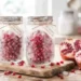 Primo piano luminoso di due barattoli di vetro congelati e ricoperti di brina, riempiti di chicchi di melograno. I barattoli poggiano su un tagliere di legno chiaro e hanno etichette con spago