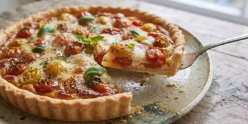 Primo piano ravvicinato di una crostata salata rustica appena sfornata con pomodorini cotti e formaggio fuso, adagiata su un piatto di ceramica ruvida sopra un tavolo in legno