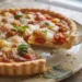Primo piano ravvicinato di una crostata salata rustica appena sfornata con pomodorini cotti e formaggio fuso, adagiata su un piatto di ceramica ruvida sopra un tavolo in legno