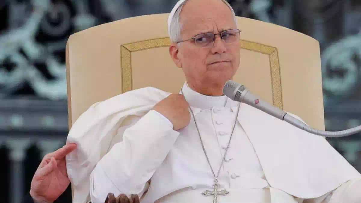 Papa Leone XIV durante un intervento pubblico in Vaticano, seduto su una poltrona chiara e con un microfono davanti, mentre parla ai fedeli in occasione dell'Angelus