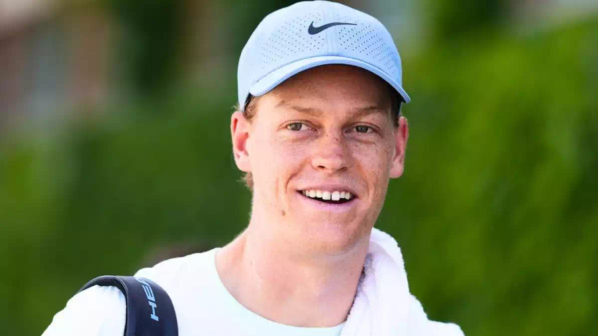 Jannik Sinner in primo piano con cappellino chiaro durante un torneo di tennis, dopo l'annuncio dello stop alla stagione 2026 per curare il problema al ginocchio
