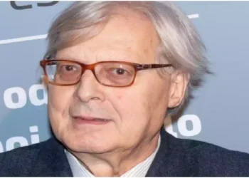 Vittorio Sgarbi durante un evento pubblico in un primo piano fotografico, con occhiali dalla montatura scura e giacca elegante
