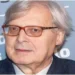 Vittorio Sgarbi durante un evento pubblico in un primo piano fotografico, con occhiali dalla montatura scura e giacca elegante