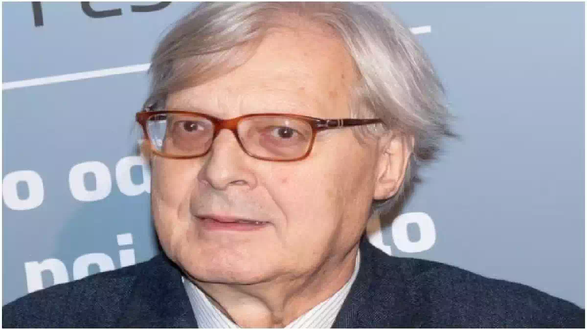 Vittorio Sgarbi durante un evento pubblico in un primo piano fotografico, con occhiali dalla montatura scura e giacca elegante