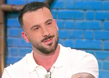 Andreas Muller in primo piano durante una puntata televisiva, con polo bianca e sfondo azzurro sfocato