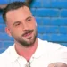 Andreas Muller in primo piano durante una puntata televisiva, con polo bianca e sfondo azzurro sfocato