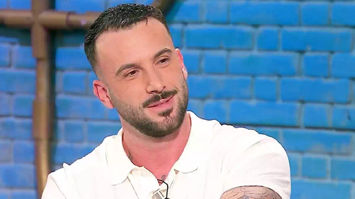 Andreas Muller in primo piano durante una puntata televisiva, con polo bianca e sfondo azzurro sfocato