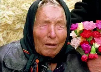 Baba Vanga durante un'apparizione pubblica, ritratta con un foulard nero sul capo e un mazzo di fiori colorati accanto, simbolo delle celebri profezie