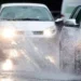 Maltempo con forte pioggia su una strada urbana: automobili in marcia tra pozzanghere e spruzzi d’acqua sull’asfalto bagnato durante un intenso temporale