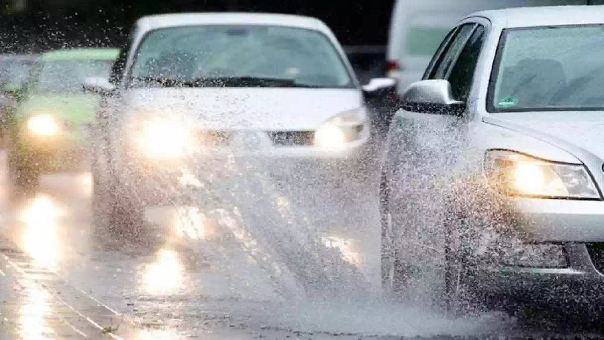 Maltempo con forte pioggia su una strada urbana: automobili in marcia tra pozzanghere e spruzzi d’acqua sull’asfalto bagnato durante un intenso temporale