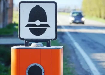 Autovelox installato sul bordo di una strada extraurbana mentre un'automobile si avvicina in lontananza, immagine simbolo delle nuove regole del Codice della Strada e delle sanzioni per eccesso di velocità