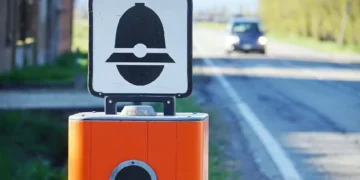 Autovelox installato sul bordo di una strada extraurbana mentre un'automobile si avvicina in lontananza, immagine simbolo delle nuove regole del Codice della Strada e delle sanzioni per eccesso di velocità