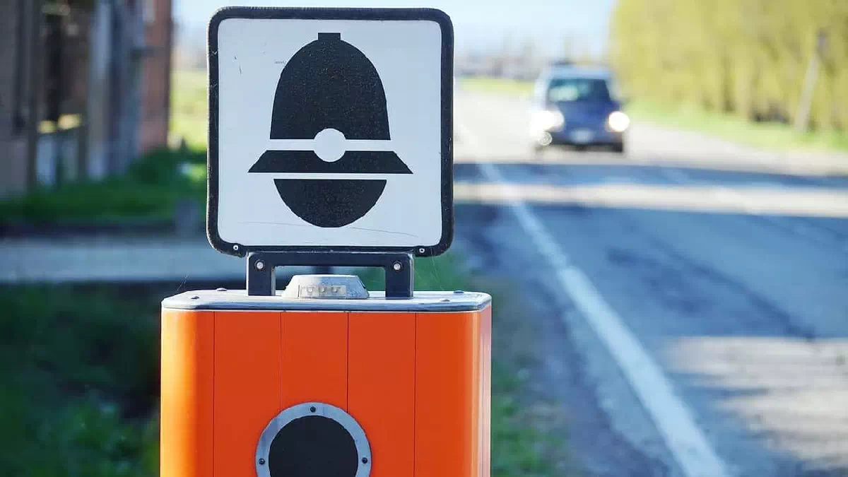 Autovelox installato sul bordo di una strada extraurbana mentre un'automobile si avvicina in lontananza, immagine simbolo delle nuove regole del Codice della Strada e delle sanzioni per eccesso di velocità
